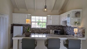 Cocina con gabinetes blancos, una isla central con taburetes altos y una lámpara colgante, además de un ventanal que proporciona luz natural.