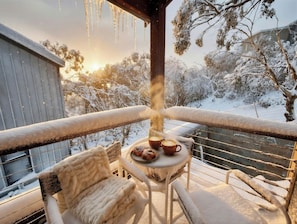 Ein Balkon mit Tisch für zwei Personen, einem Stuhl und Blick auf schneebedeckte Bäume und ein Gebäude.