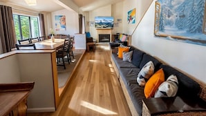A spacious living area with a wooden floor, a sofa with cushions, a dining table with chairs, and a fireplace. - Glacier Chalet - Luxury Mt Buller Ski Chalet • Fireplace •Sleeps 14 (Mount Buller)