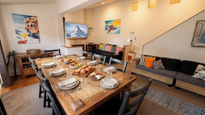 A dining area with a wooden table set for a meal, a sofa, and a TV mounted on the wall. - Glacier Chalet - Luxury Mt Buller Ski Chalet • Fireplace •Sleeps 14 (Mount Buller)