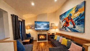 A cozy living room with a fireplace, a television, and a large painting of a skier. - Glacier Chalet - Luxury Mt Buller Ski Chalet • Fireplace •Sleeps 14 (Mount Buller)