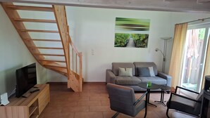 A living room with a wooden staircase, a sofa, a coffee table, a TV, and a fireplace. - Luxury holiday home with every comfort - sauna, bathtub with whirlpool function (Nordhorn)