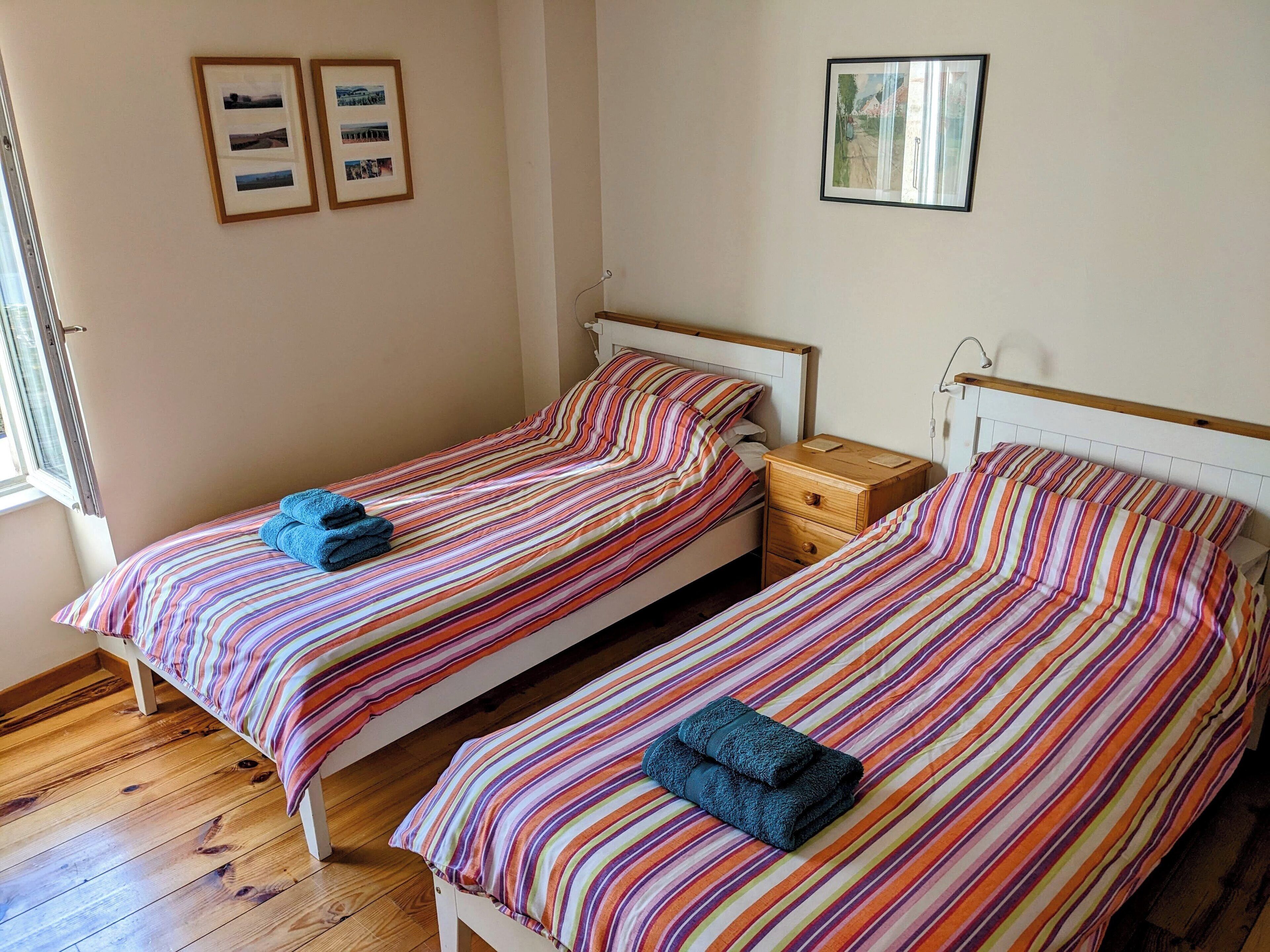 A room with two single beds, wooden flooring, and framed pictures on the walls.