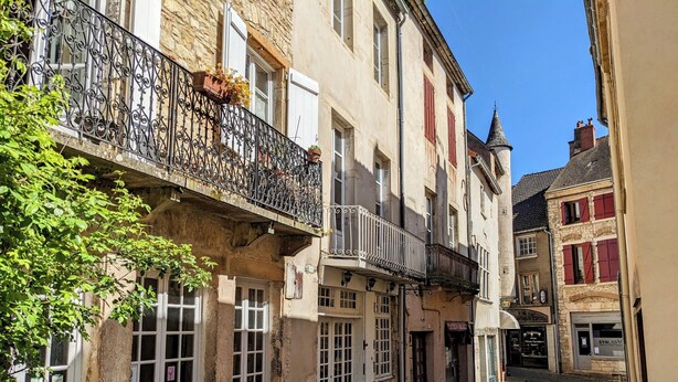 A narrow cobblestone street lined with historic buildings, featuring balconies with wrought iron railings and flower boxes.