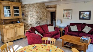 A cozy living room with a stone wall, a wooden cabinet, a red sofa set, a wooden table, and a patterned tablecloth.