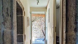 A narrow stone-walled hallway leading to a wooden staircase and a stone wall outside.