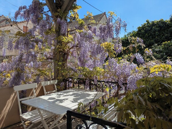 A patio with a white table and chairs, surrounded by purple wisteria vines and a brick wall.