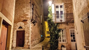 A narrow cobblestone alleyway between buildings with stone facades, a small tree, and a lit street lamp.
