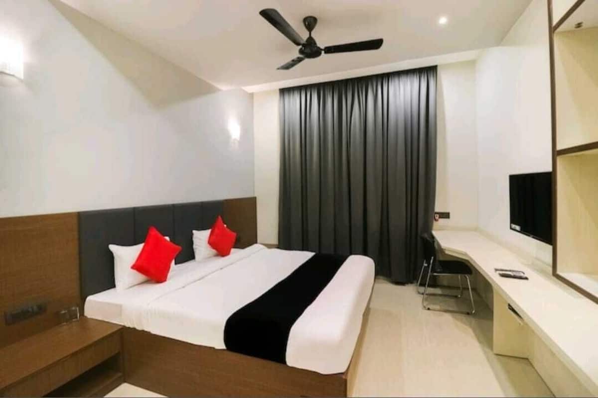 Una habitación de hotel con una cama, un escritorio, una silla, un televisor y un ventilador de techo.