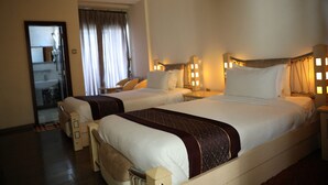 Une chambre d’hôtel avec deux lits, un coin salon et une salle de bain visible à travers une porte en verre.