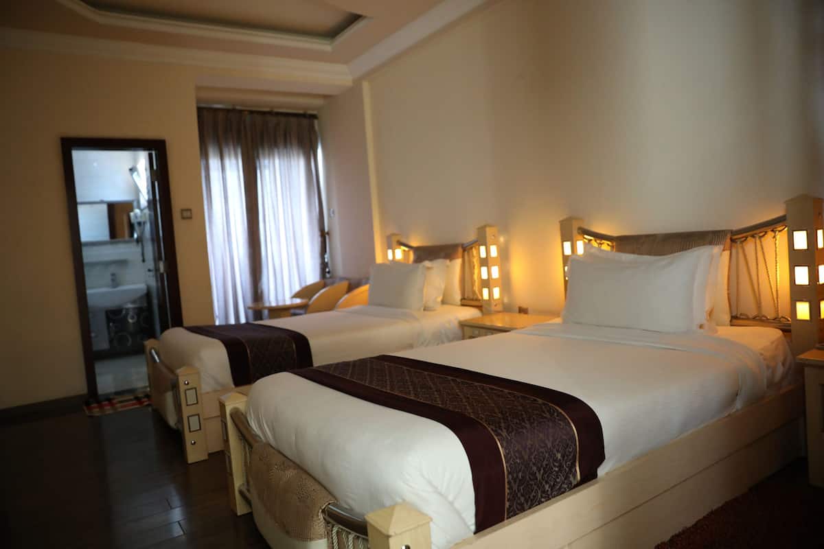 A hotel room with two beds, a sitting area, and a bathroom visible through a glass door.