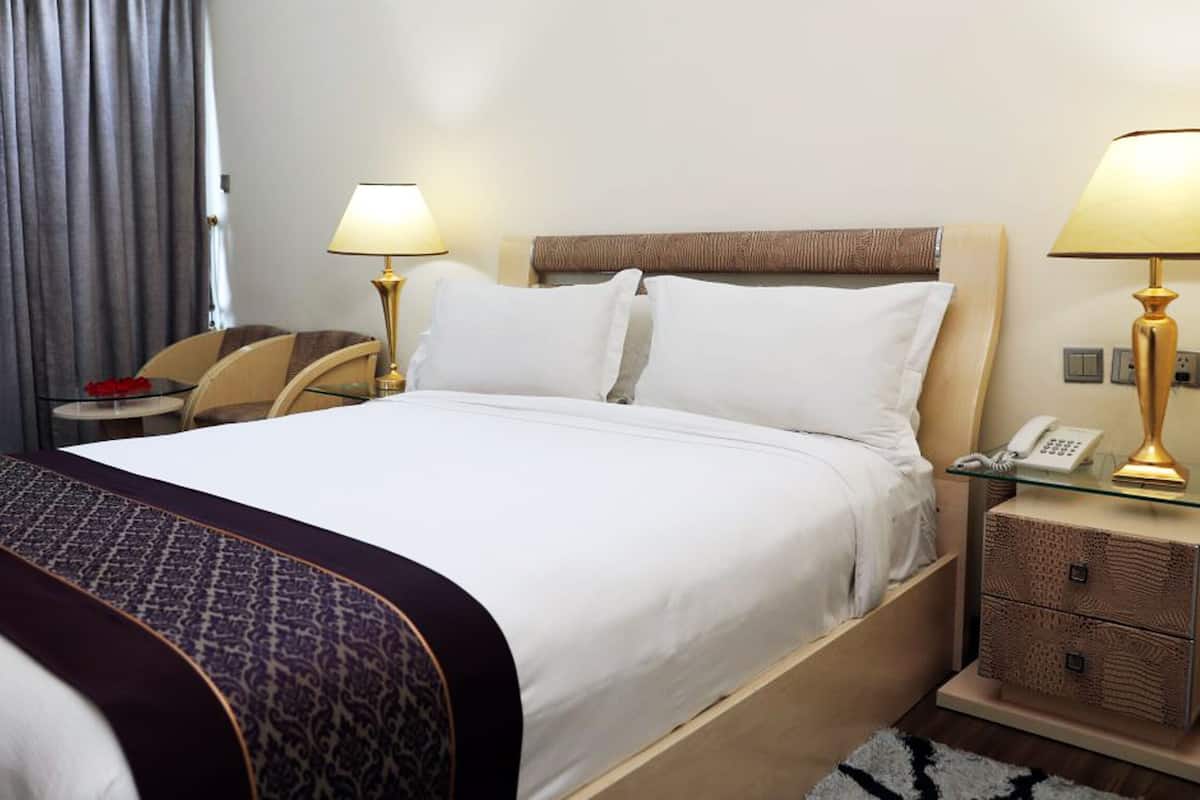 A hotel room with a large bed, two bedside lamps, a bedside telephone, a small table with a red object, and a nightstand with a lamp and a phone.