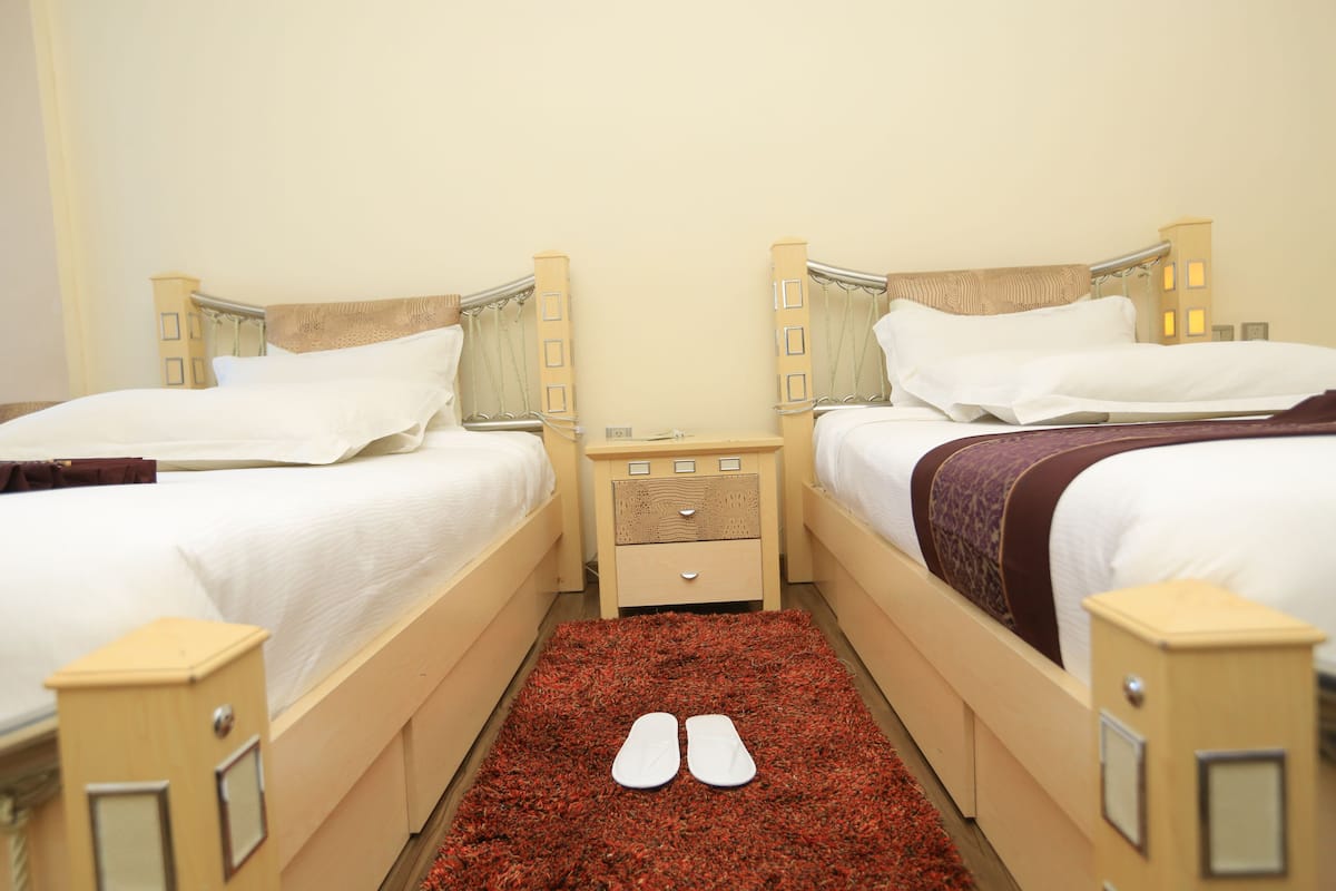 A hotel room with two beds, a small bedside table, and a red carpet.