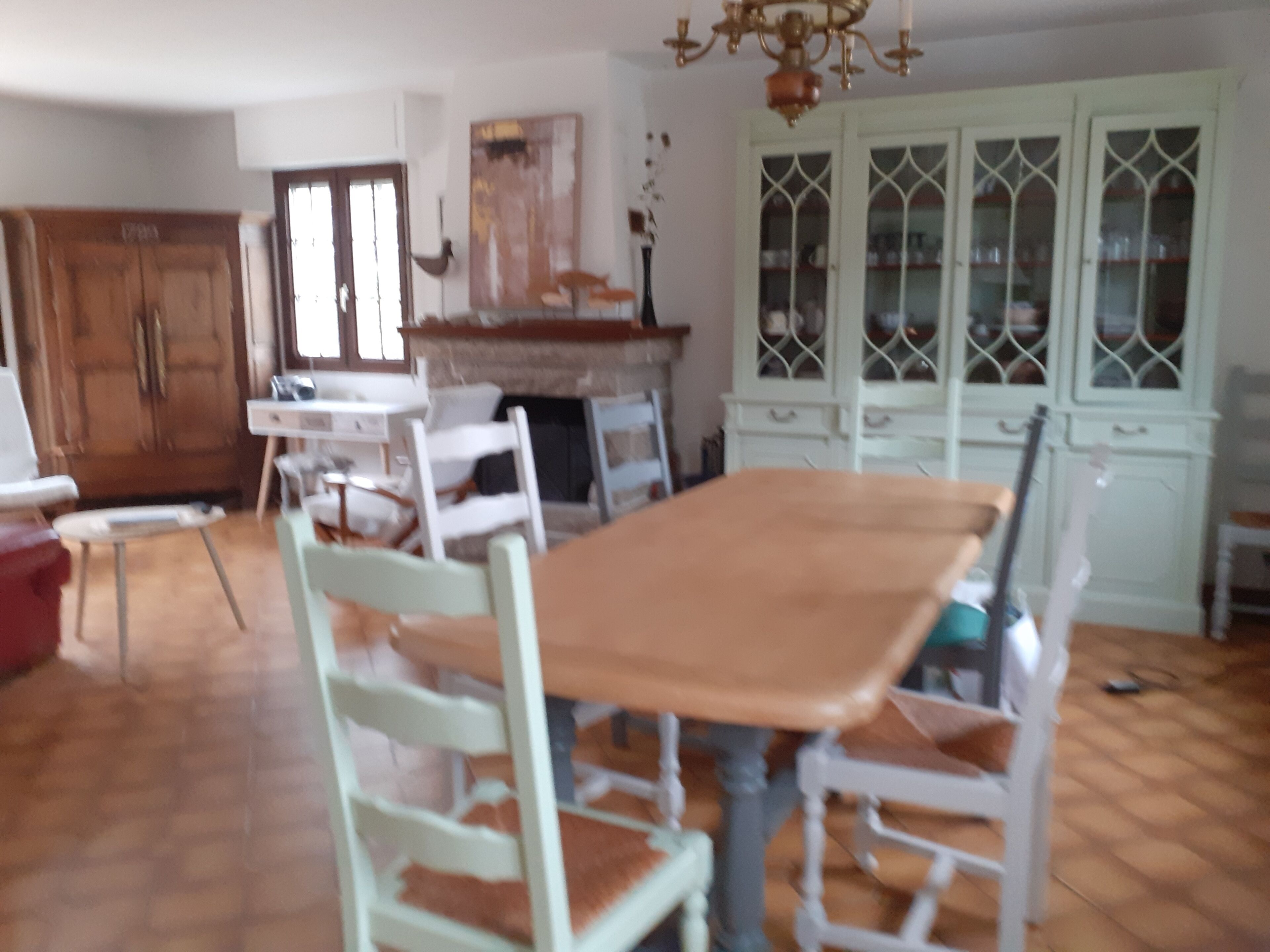 Uma sala de jantar com mesa de madeira e cadeiras brancas, lareira e armário com portas de vidro.