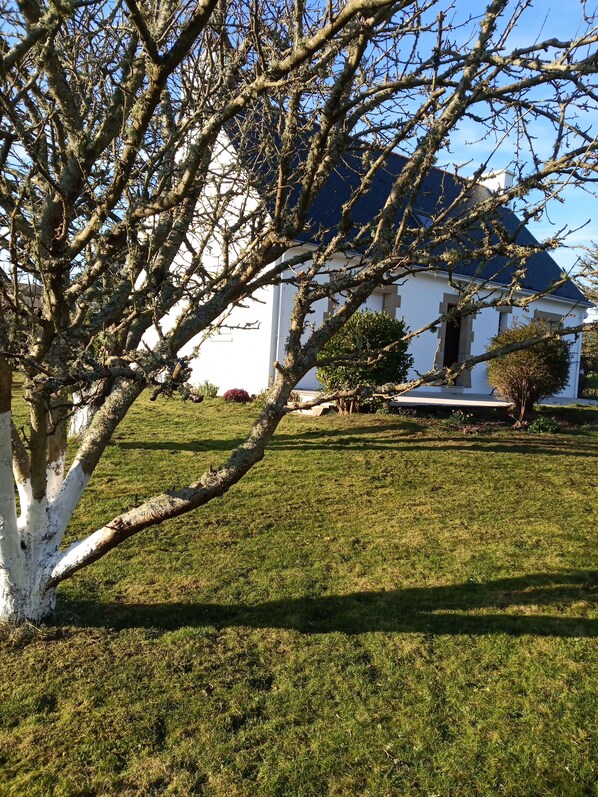 A white house with a dark roof, surrounded by a well-maintained lawn and a tree with bare branches.