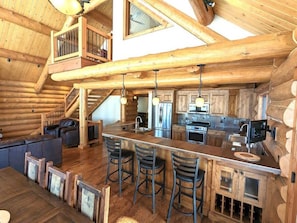 A log cabin interior with a kitchen, dining area, and a loft bedroom.