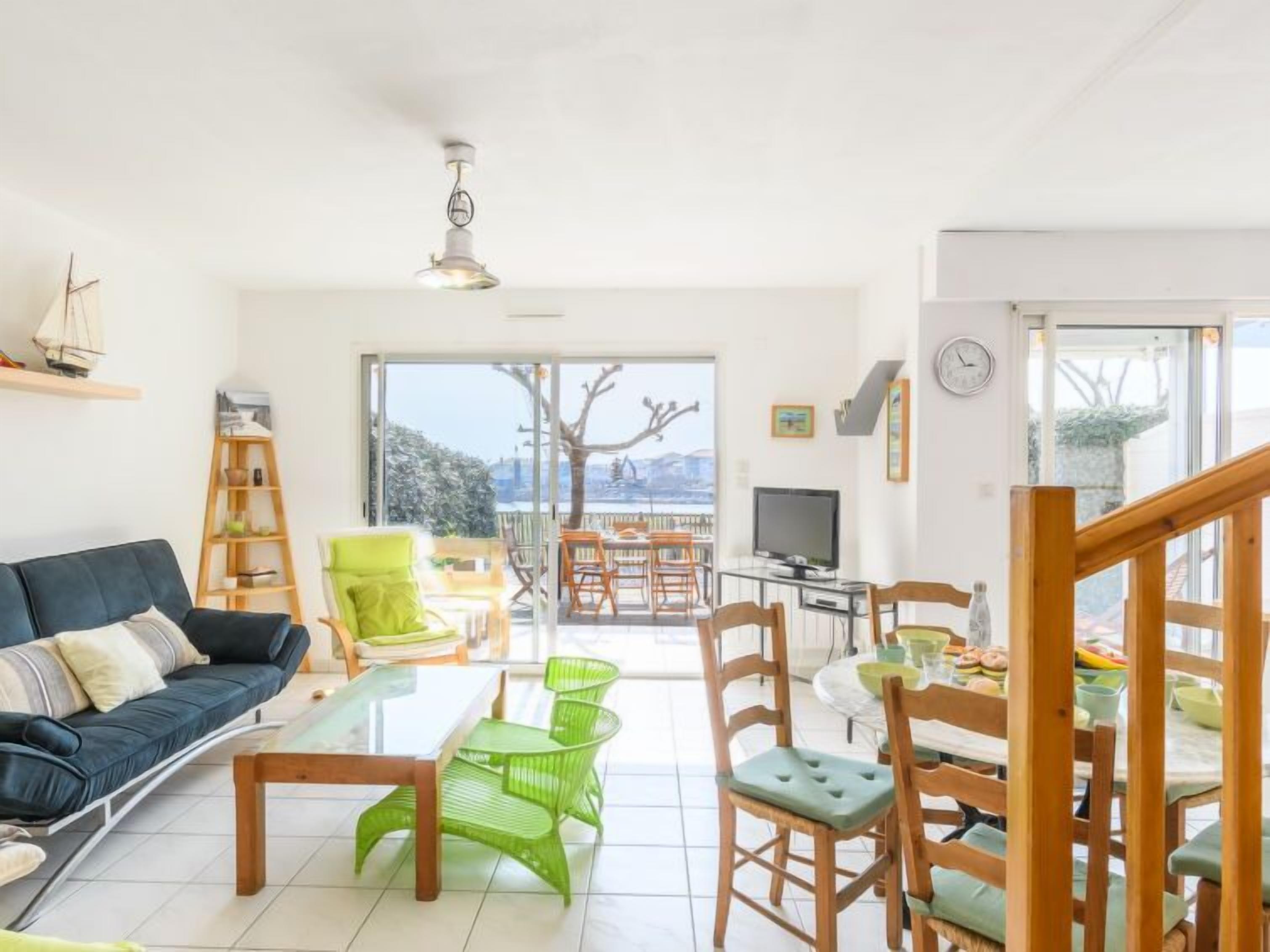 A bright living room with a sofa, a coffee table, and a TV. There is a balcony with a view of the city.