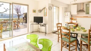 Un vaste espace de vie comprenant un grand salon avec une grande porte-fenêtre coulissante donnant sur un balcon, un téléviseur posé sur un meuble et une table à manger avec des chaises.