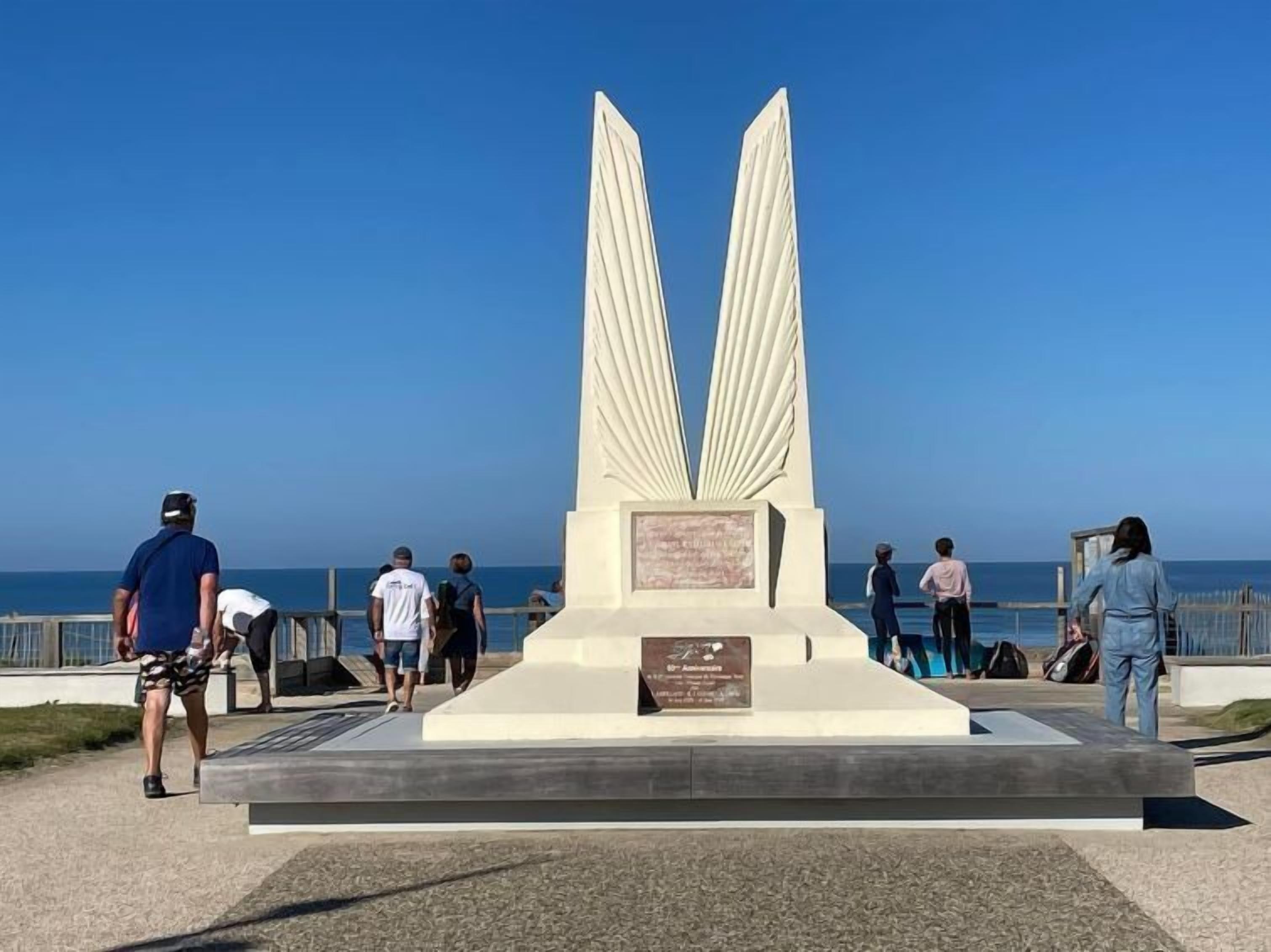 Een monument met twee grote vleugels, omringd door een verharde looppad, met een helder zicht op de oceaan op de achtergrond.