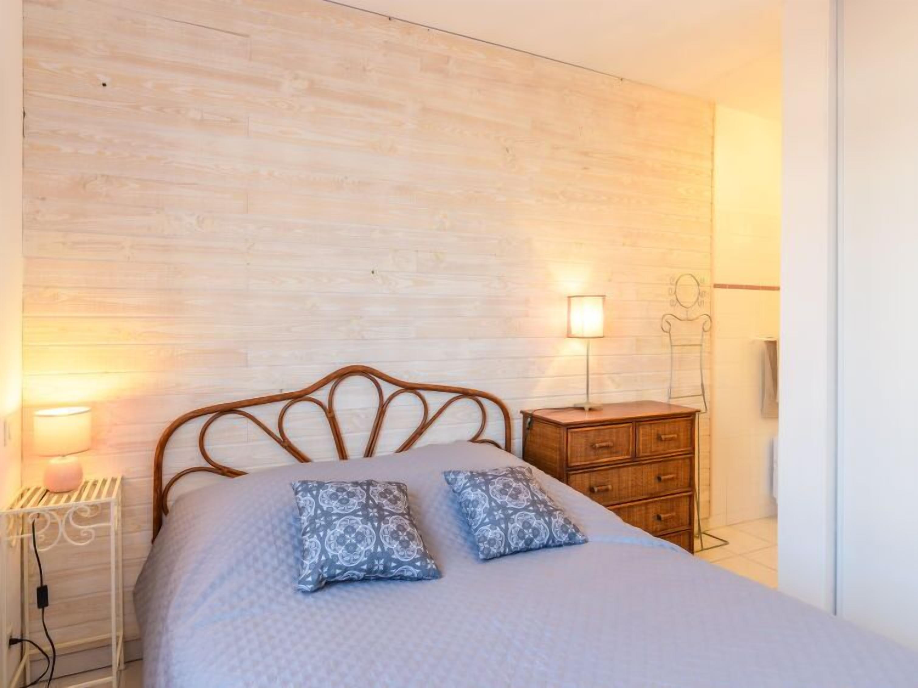 A bedroom with a wooden headboard, two bedside lamps, a wooden dresser, and a patterned bedspread.