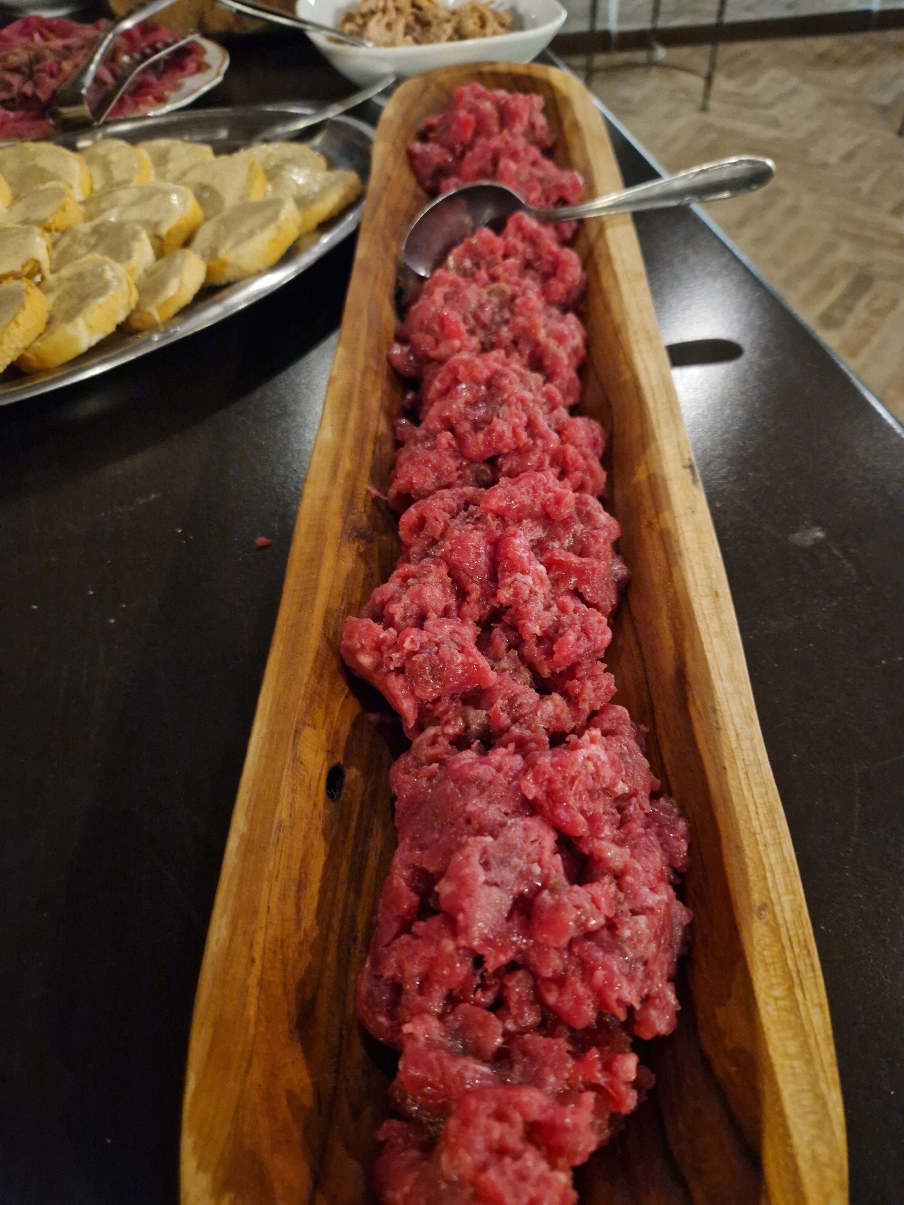 Een houten serveerplank met rauw vlees en plakjes brood op een tafel.