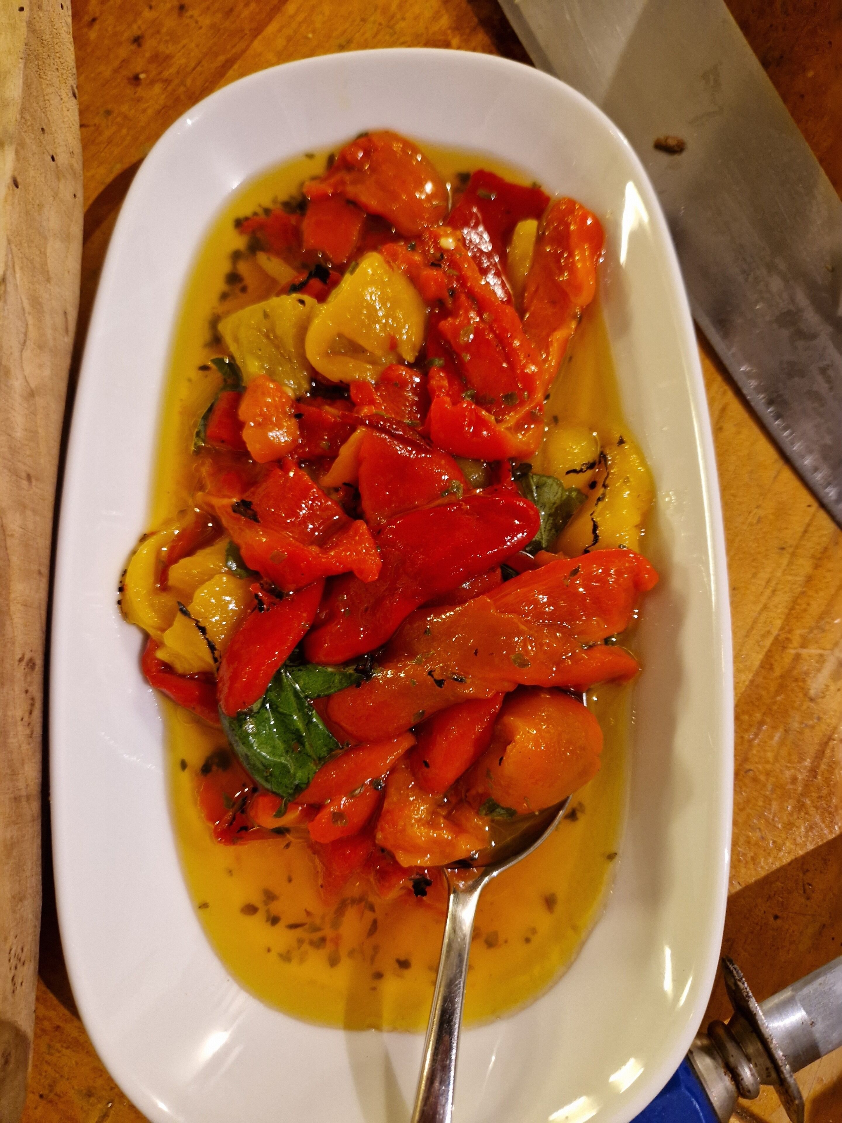 Een wit, ovaal bord met roerbakgroenten, waaronder rode en gele paprika's, en een lepel.