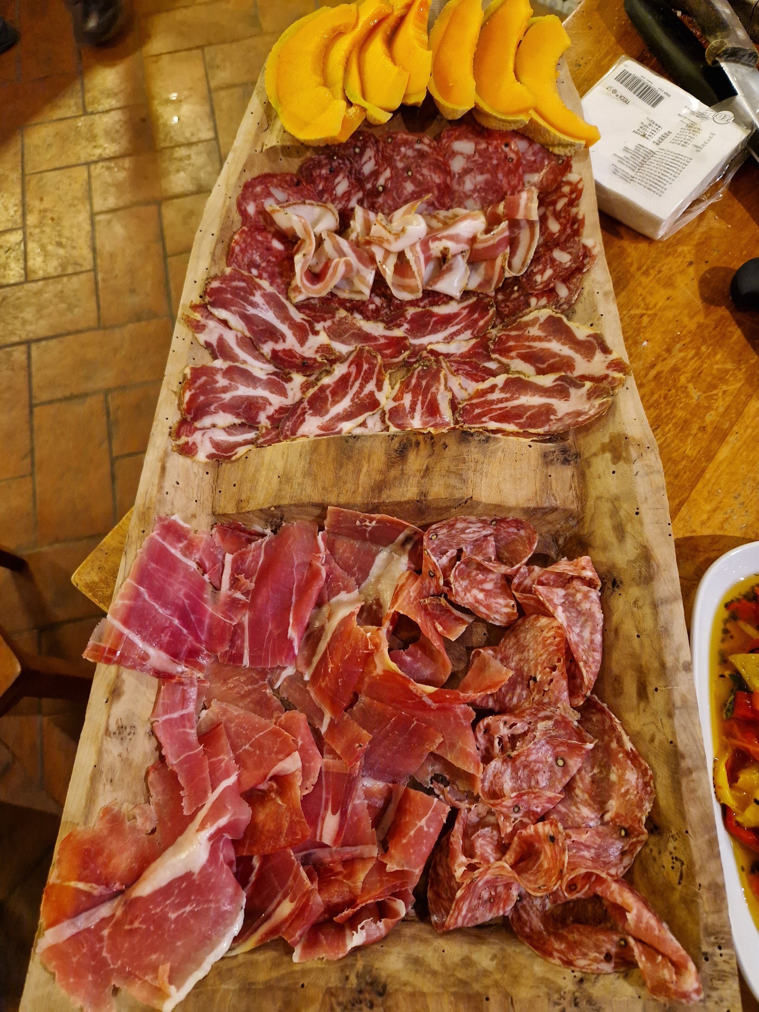 A wooden cutting board with various types of cured meats and sliced mangoes.