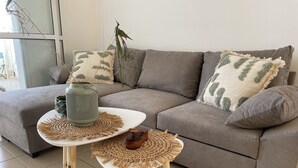 Ein modernes Wohnzimmer mit einem grauen Sofa, zwei weißen Beistelltischen mit gewebten Unterlagen und dekorativen Kissen.