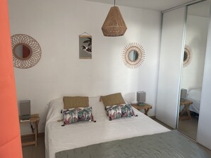 A bedroom with a large bed, two wall-mounted mirrors, and a hanging light fixture. - Accommodation with private beach access (Sainte-Anne)