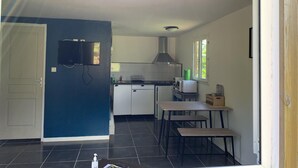 Cozinha compacta com micro-ondas, pia e fogão. Possui um espaço de refeições com mesa e bancos.