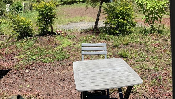 Conjunto de mesa e cadeira ao ar livre, com vista para uma encosta arborizada e uma montanha ao fundo.