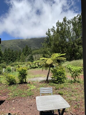 Conjunto de mesa e cadeira ao ar livre, com vista para uma encosta arborizada e uma montanha ao fundo.