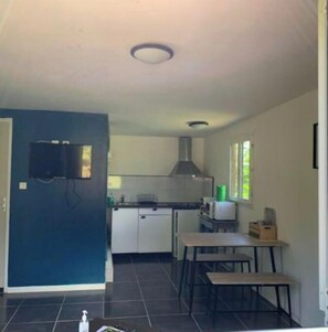Cozinha compacta com armários brancos, fogão e micro-ondas. Há uma pequena área de refeições com mesa e banco.