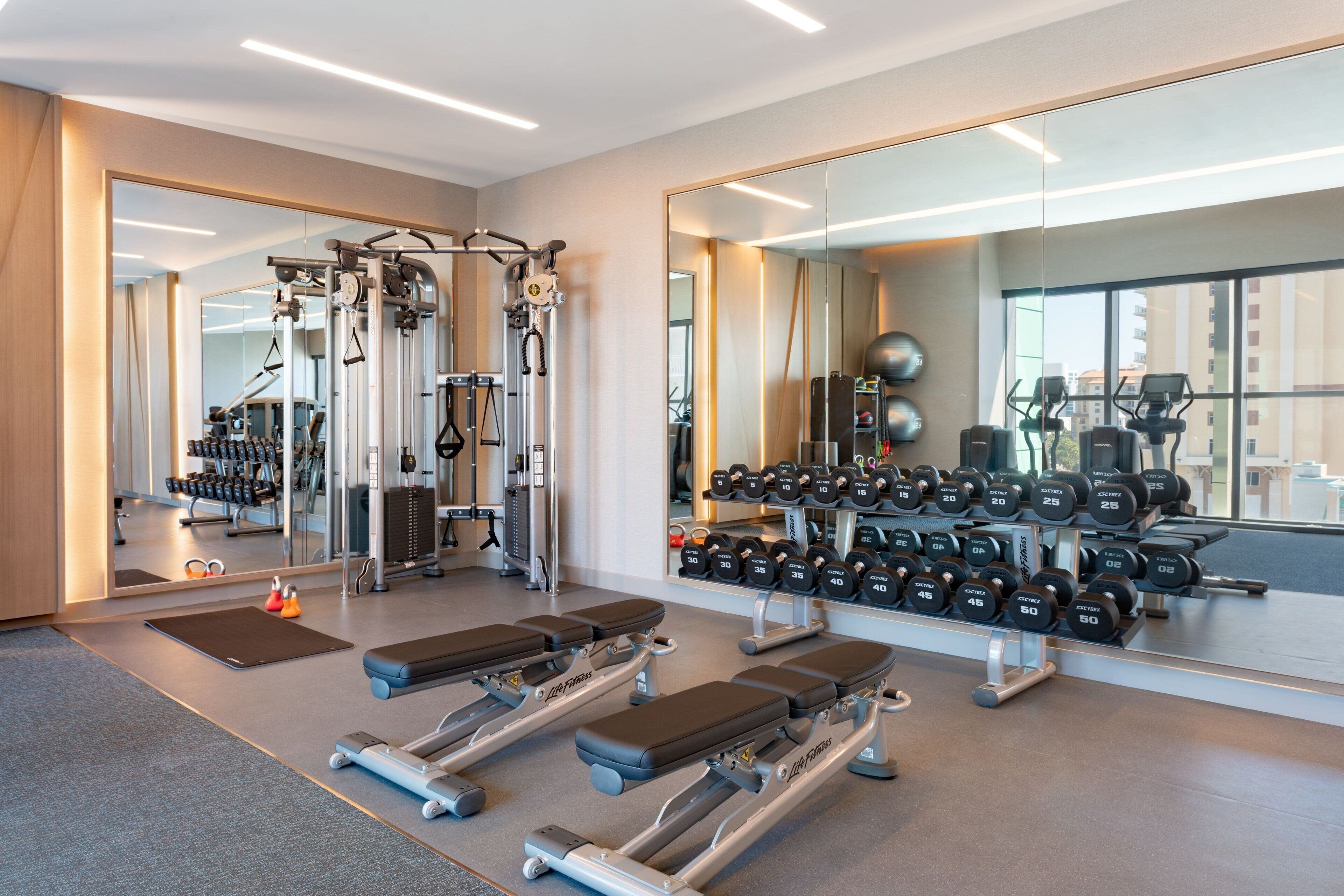 Un gimnasio moderno con equipo cardiovascular, bancos de pesas y una barra de mancuernas.