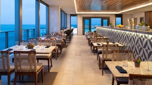 A modern restaurant with a view of the ocean, featuring wooden tables and chairs, a bar area, and large windows. - JW Marriott Clearwater Beach Resort & Spa (Clearwater Beach)