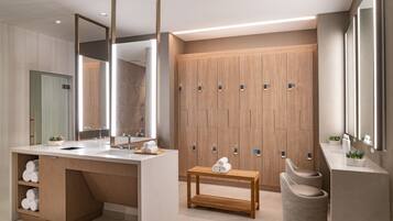 Un baño moderno con un espejo grande, taquillas de madera, un lavamanos con toallas y una mesita con toallas.