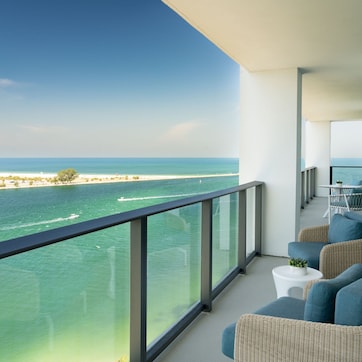 A balcony with wicker furniture, a small table, and a view of the ocean and beach.