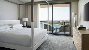 Habitación de hotel con una cama grande, un balcón con vistas al mar, un televisor y un aparador de madera.