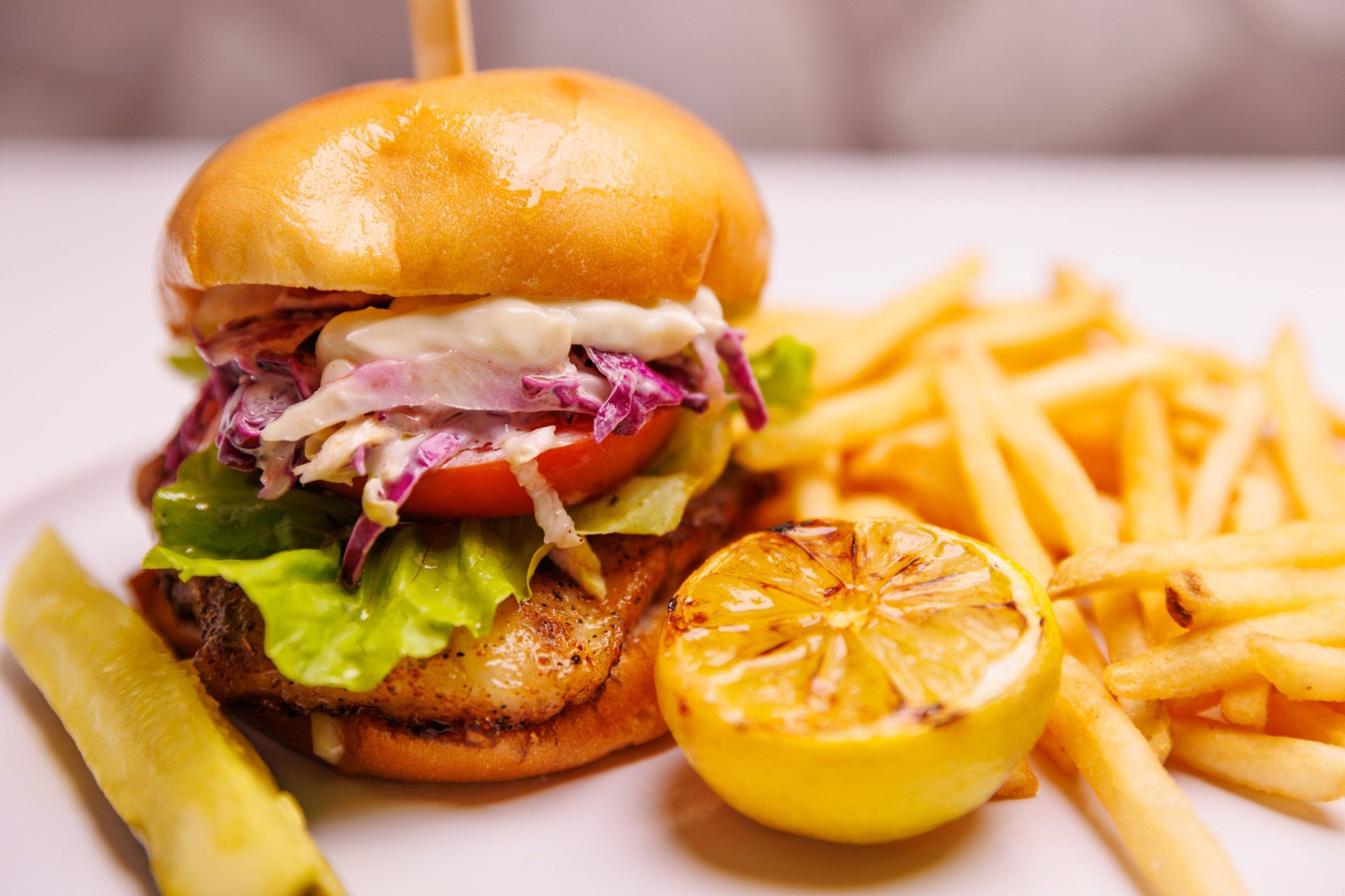 Una hamburguesa con papas fritas y un gajo de limón en un plato.
