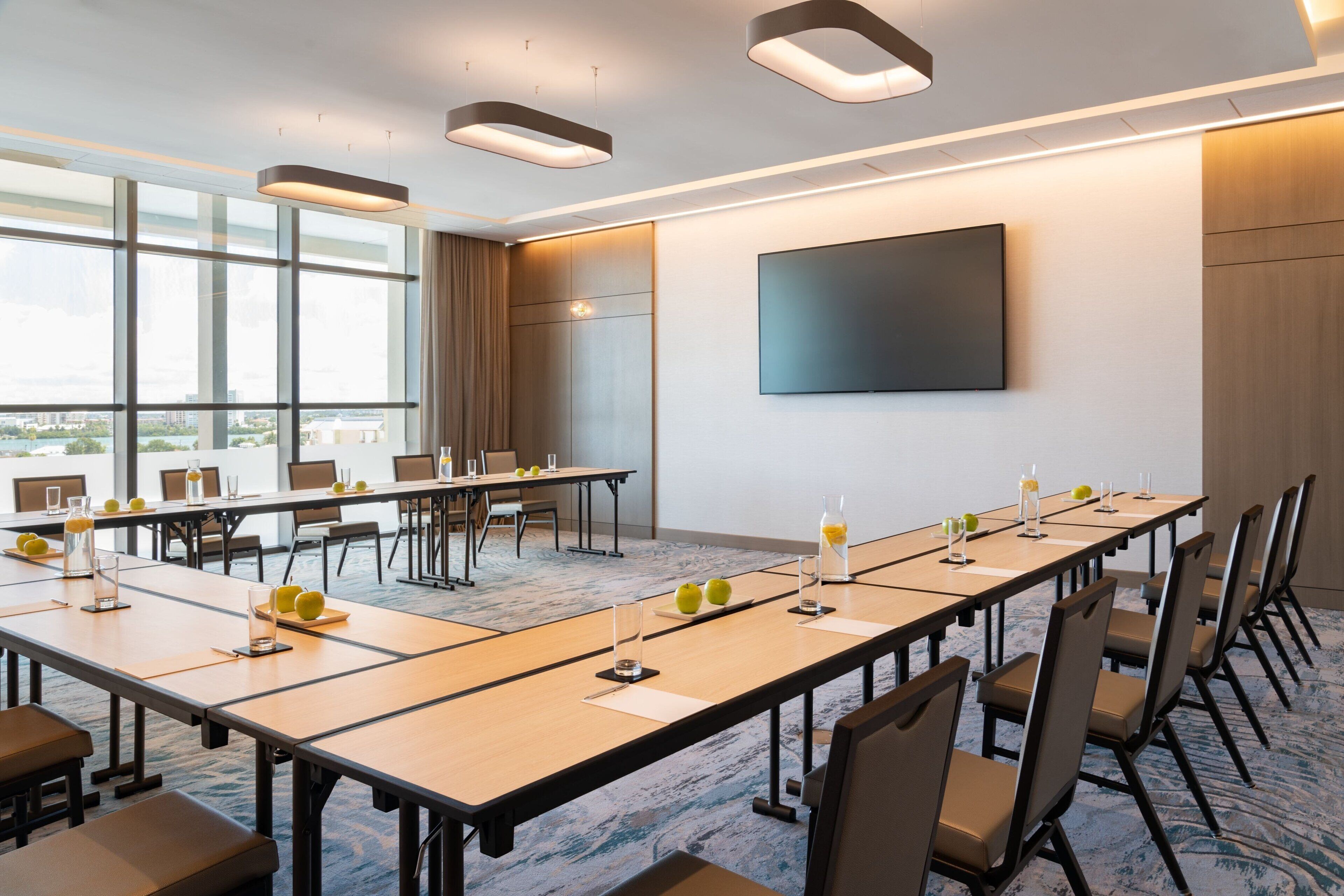 Une salle de conférence équipée de longues tables, de chaises et d’un grand écran mural.