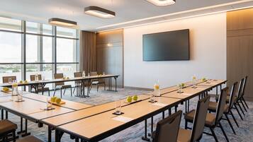 Une salle de conférence équipée de longues tables, de chaises et d’un grand écran mural.