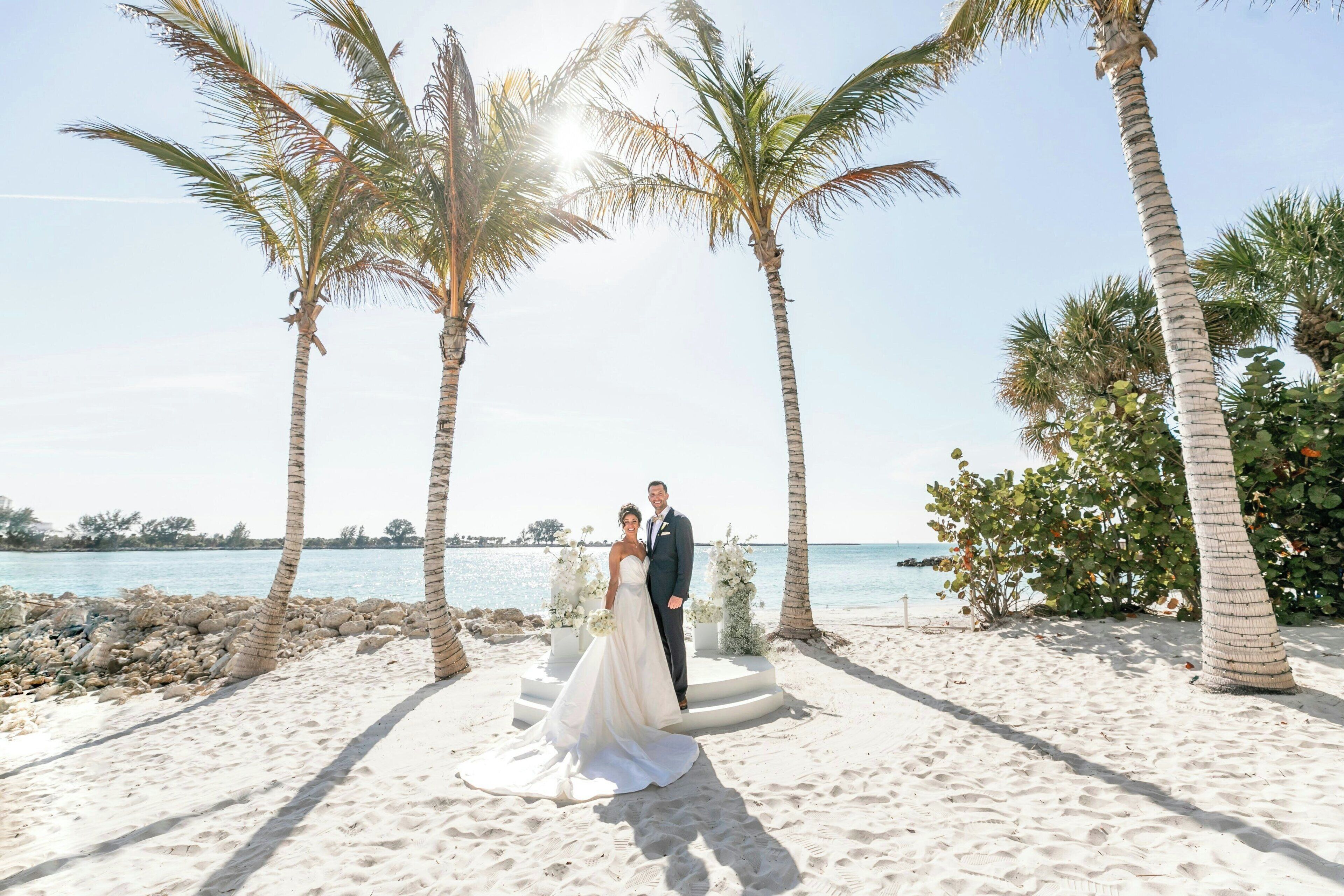 A beach wedding setup with a couple, palm trees, and a clear view of the sea.