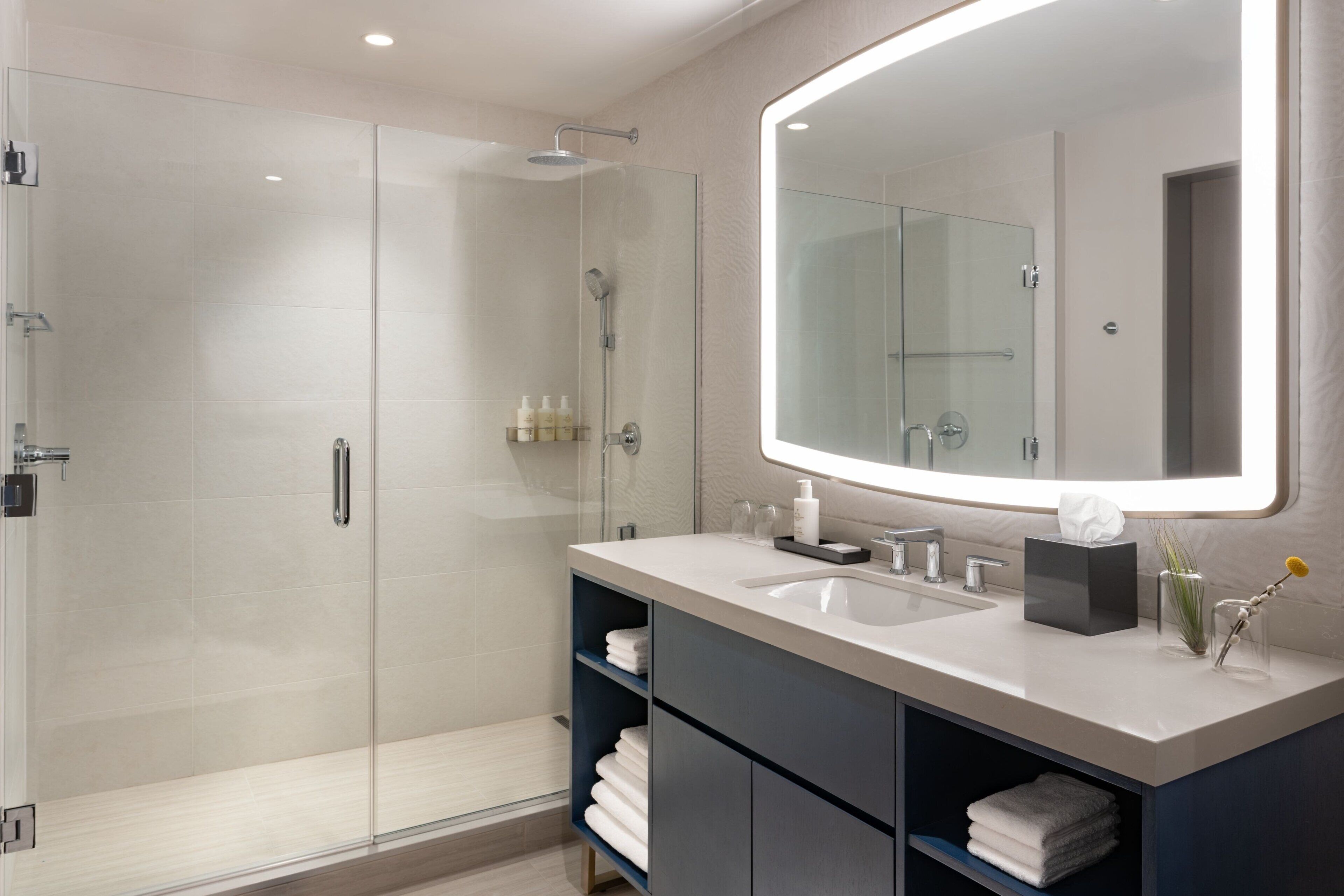 A modern bathroom with a glass-enclosed shower, a large mirror, and a vanity with a sink and storage.