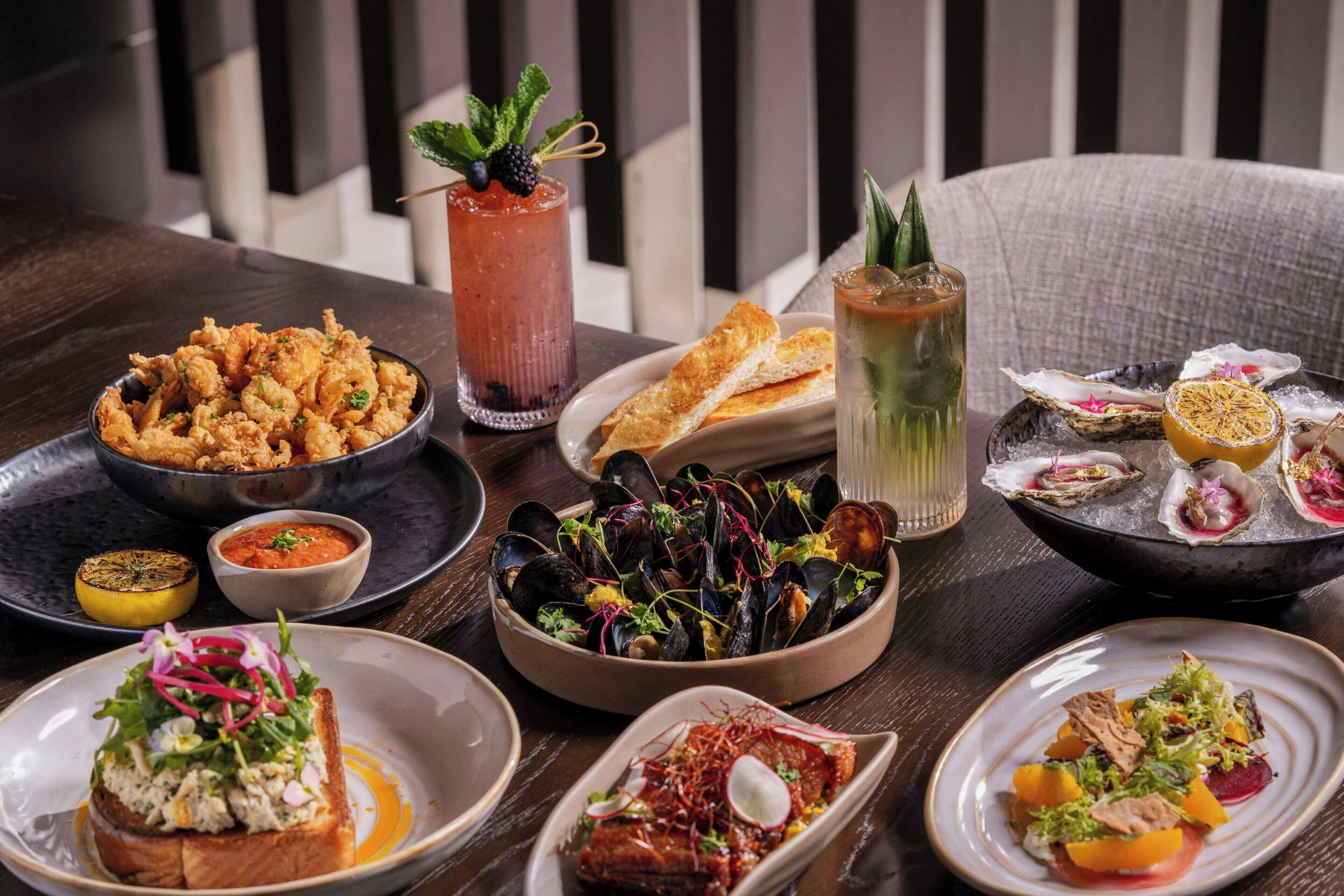 Diversos platos que incluyen mariscos, ensaladas y pan, dispuestos sobre una mesa de madera.