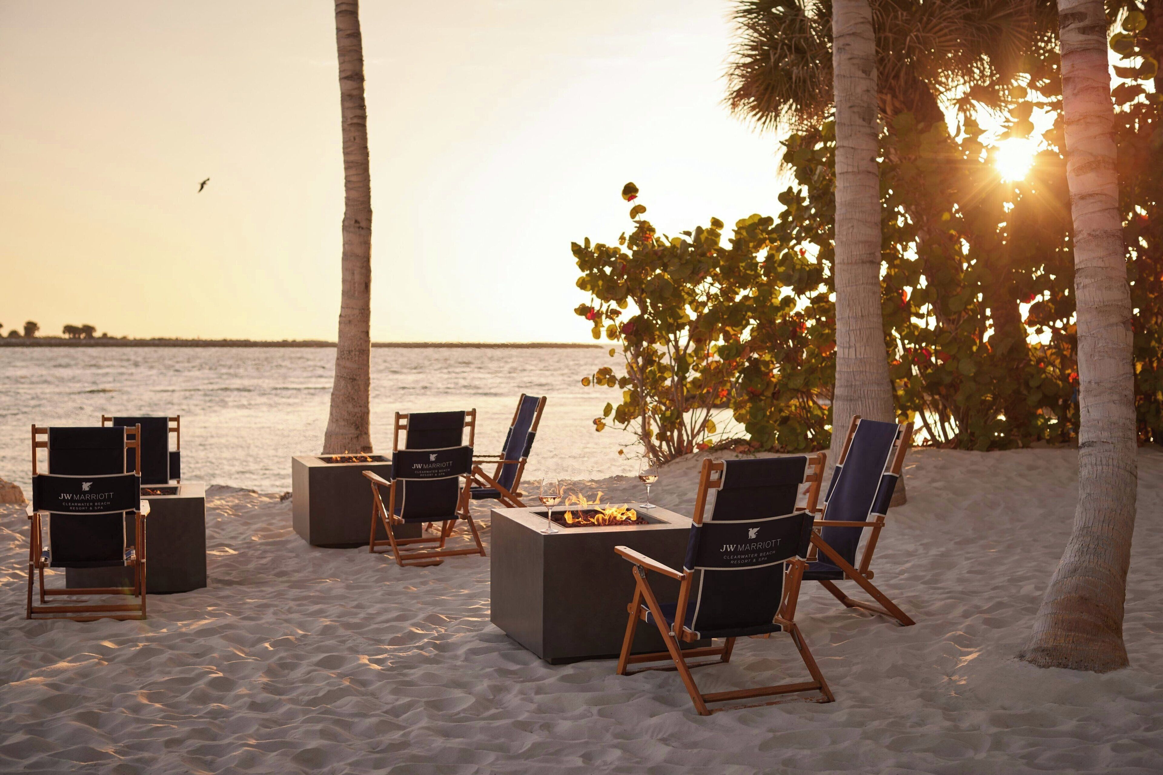 Espace extérieur aménagé avec des fauteuils confortables et un foyer, situé sur une plage de sable, avec vue sur l’océan.