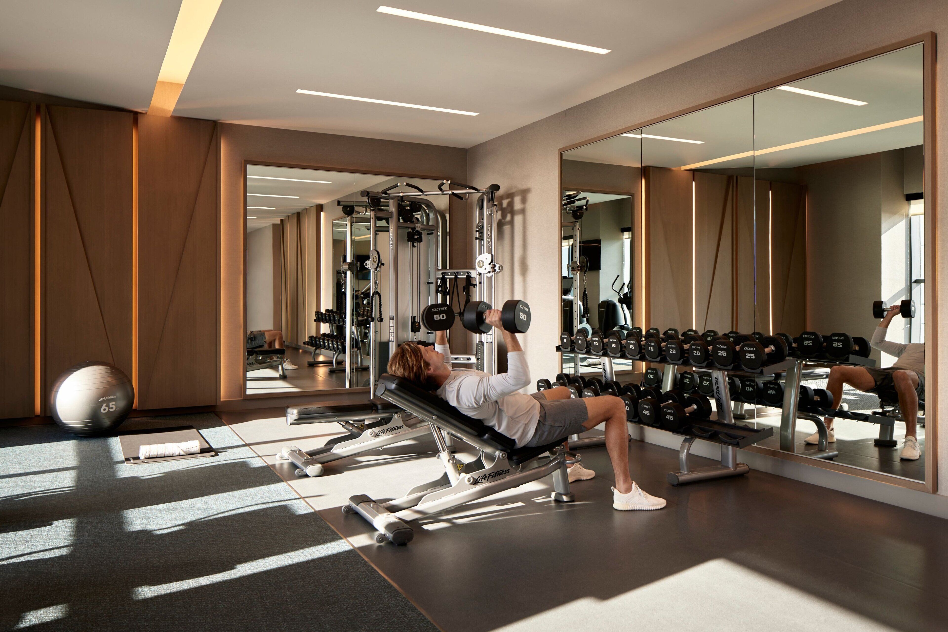 Un gimnasio moderno con varios equipos, incluyendo un banco de pesas, mancuernas y una pelota medicinal.