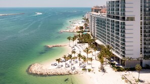 Un hotel frente al mar con playa, aguas cristalinas y un edificio moderno con balcones.