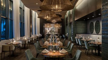 Un restaurante moderno con mesas redondas, sillas tapizadas en verde y lámparas de mimbre colgantes.