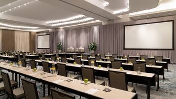 Un salón de conferencias con varias mesas, sillas y una pantalla grande.