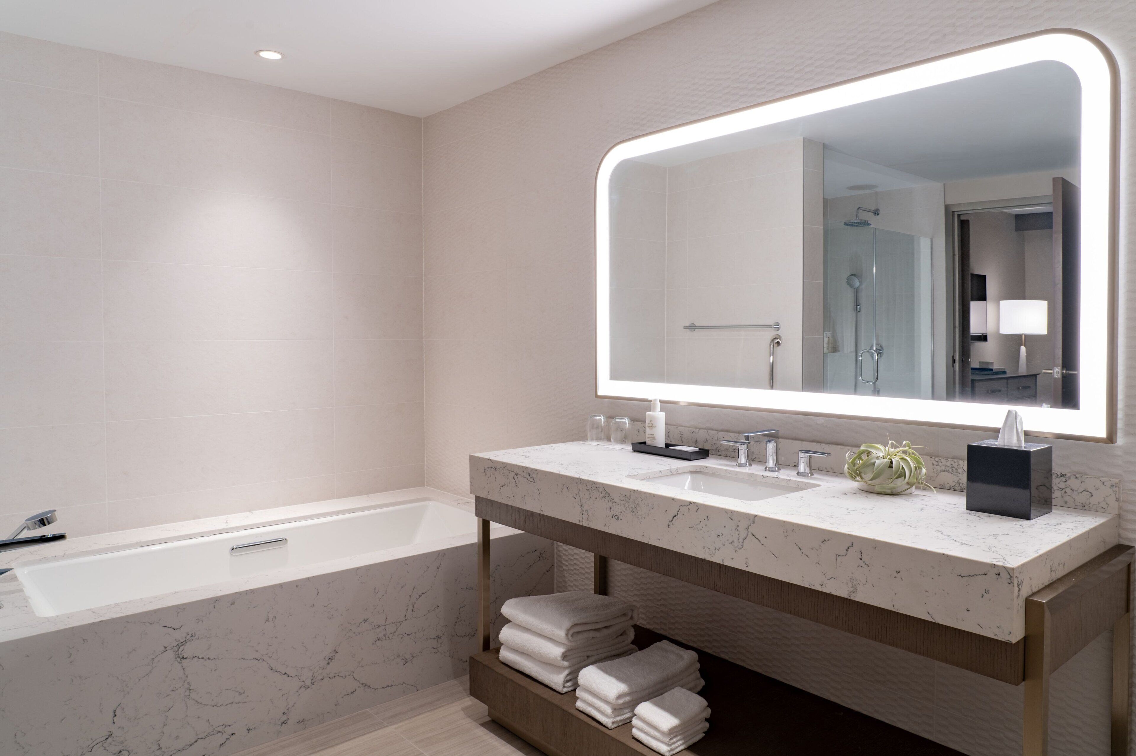 A modern bathroom with a large mirror, a bathtub, a vanity with a sink, and neatly folded towels.